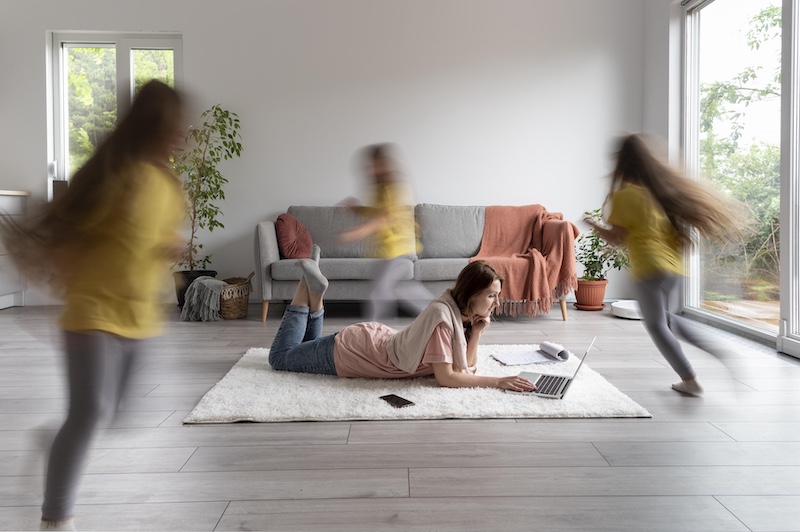 Woman trying to work with laptop from home while her children run around.